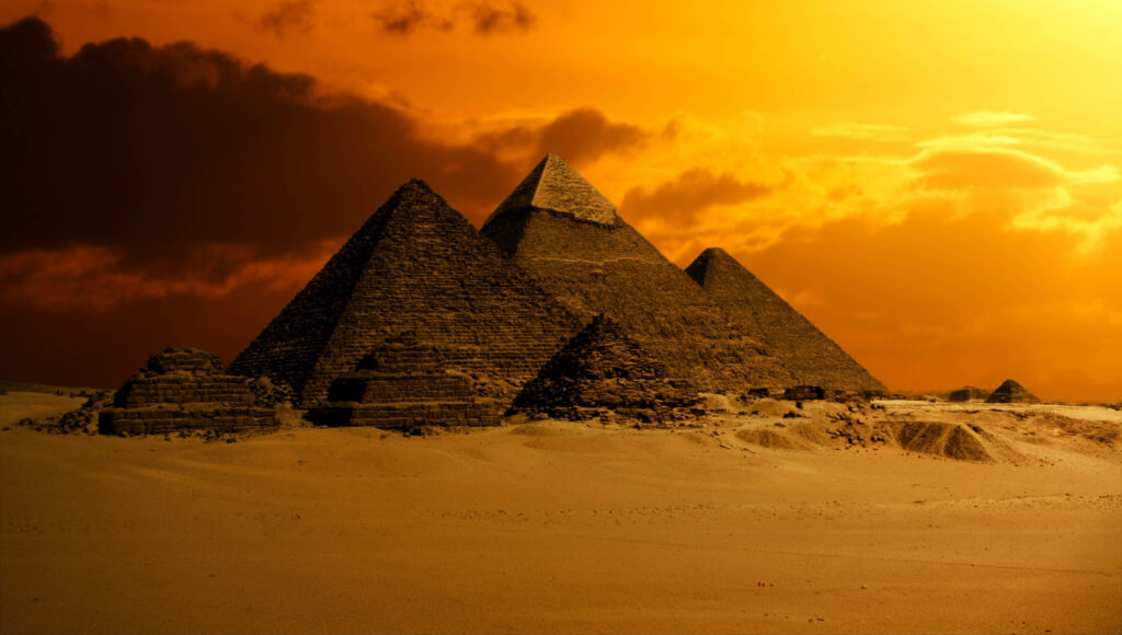 Egyptian pyramids at sunset with golden orange hues and dramatic clouds wallpaper background