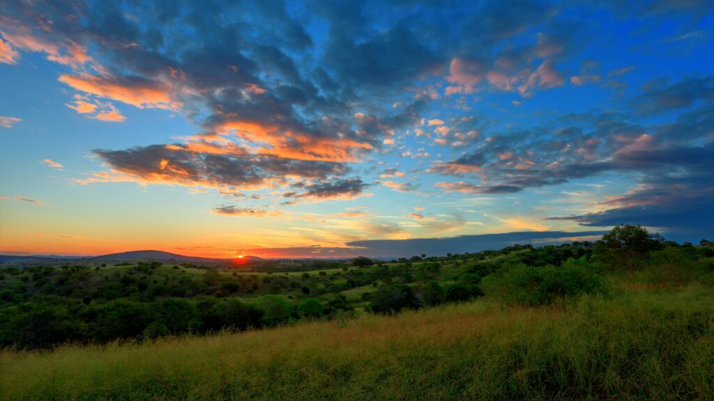 Serene sunset over lush green grassy field and rolling hills with colorful vibrant sky clouds Wallpaper