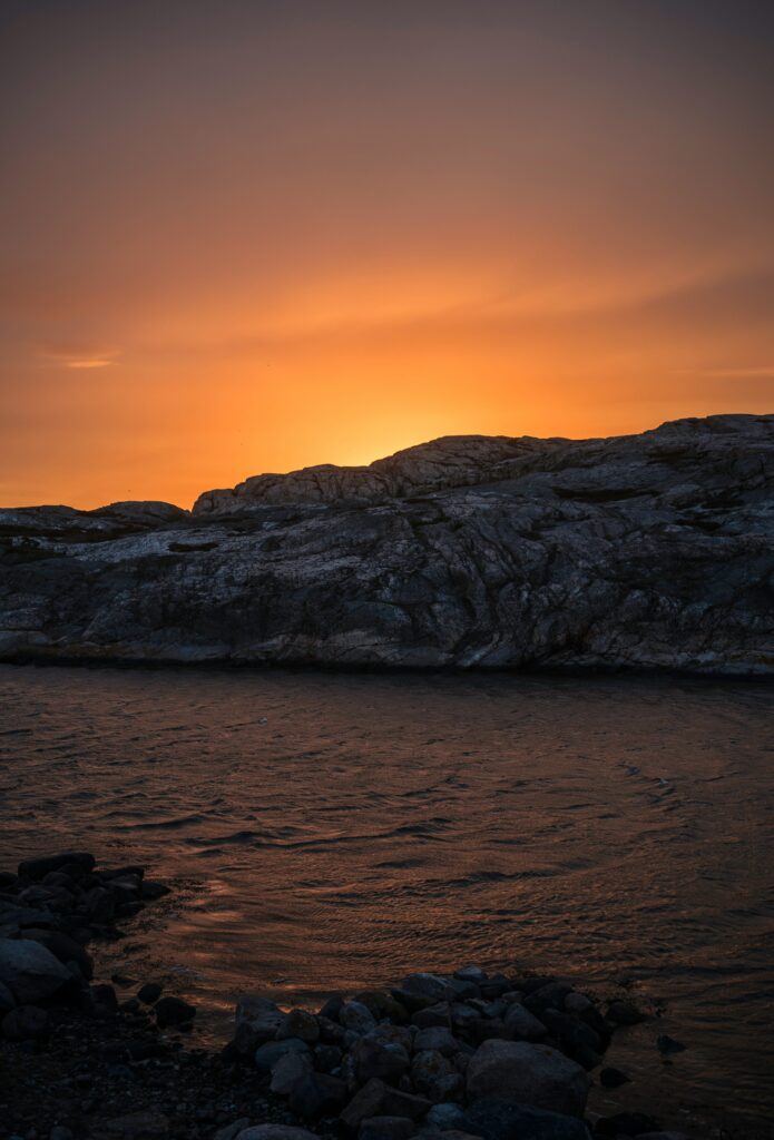 Sunset over rugged sea rocks with warm orange sky and soft water reflections wallpaper background