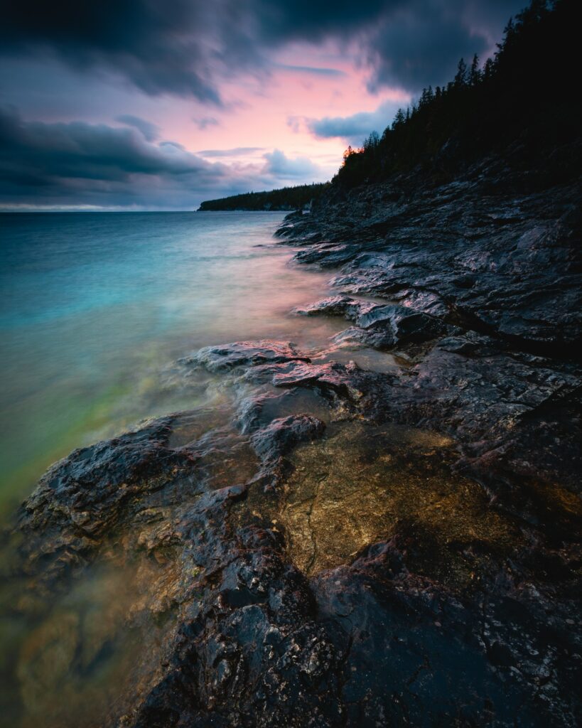 Dramatic Georgian coast bay sunset with rugged stones windswept trees and vibrant sky reflection Wallpaper