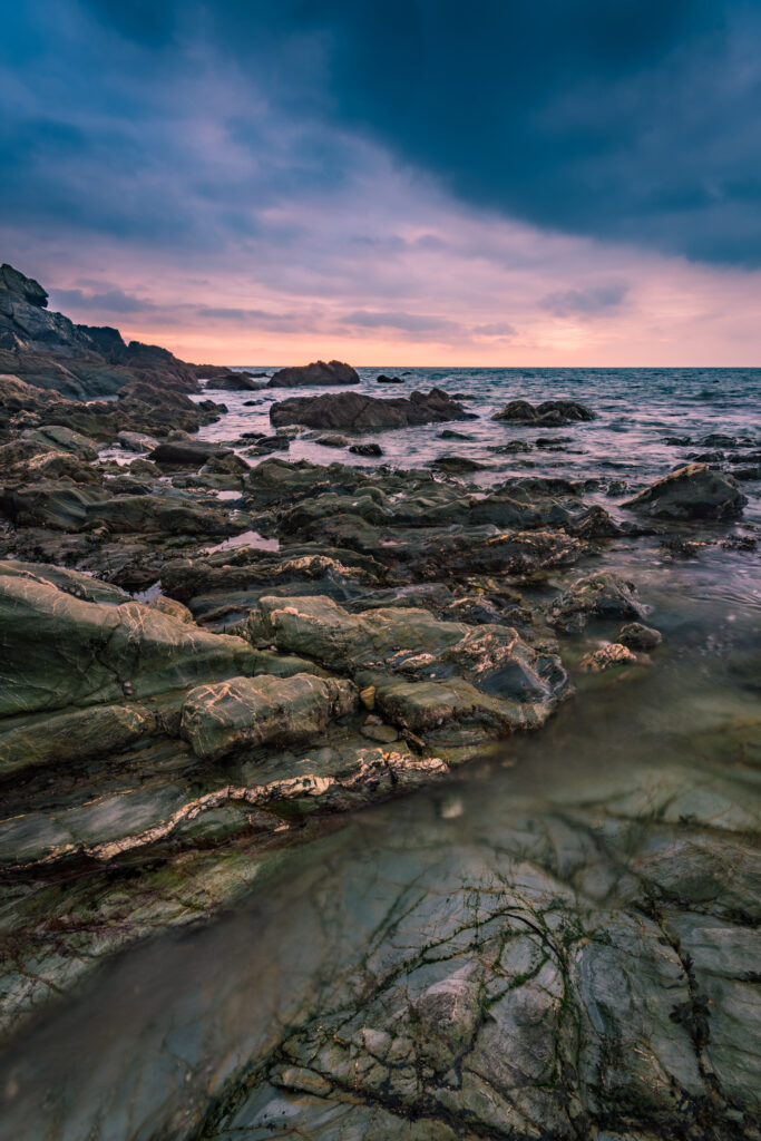 Sunset over rugged rocky shoreline with textured stones and soft orange pink sky ocean view wallpaper