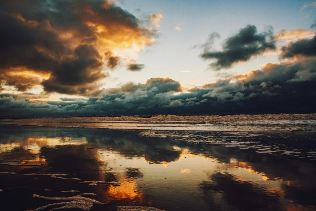 Sunset over sea with dark clouds golden sunlight reflecting on wet sand and gentle waves Wallpaper