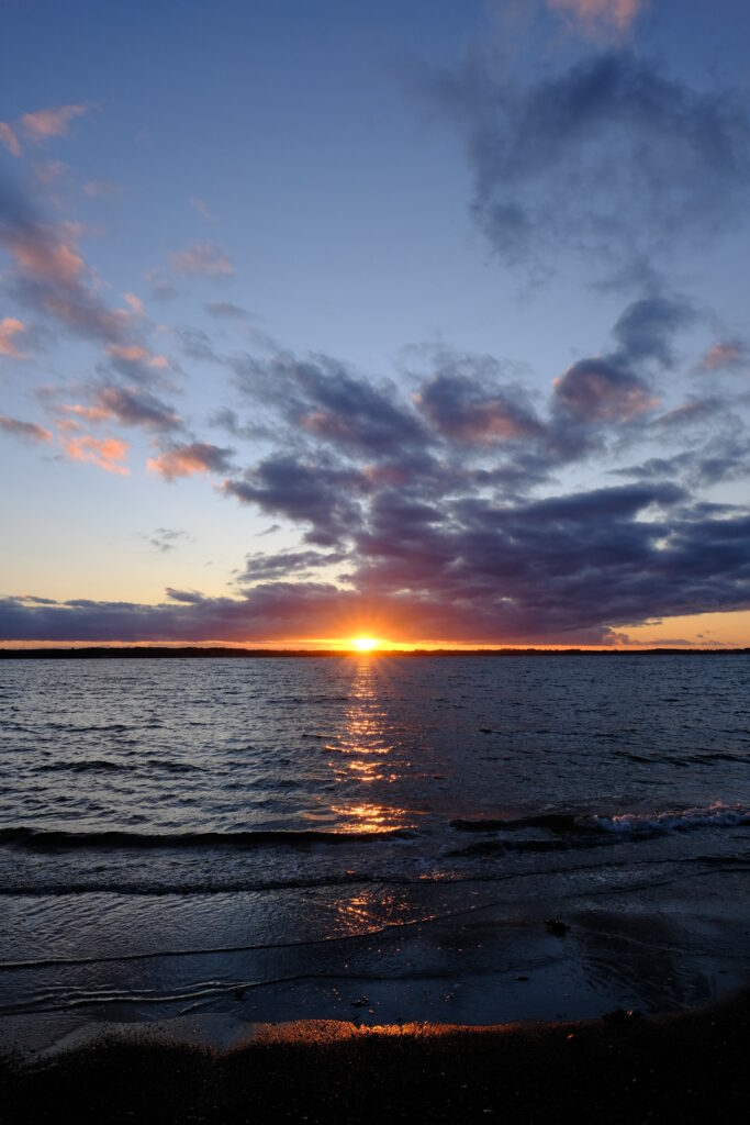 Sunset over sea with golden rays purple orange sky dramatic clouds coastal shoreline wallpaper