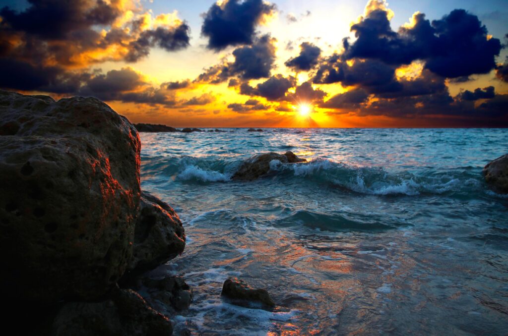Vibrant sunset over sea with glowing clouds and crashing surf on weathered coastal rocks wallpaper