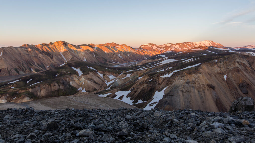 Panoramic sunset landscape with rugged hills snow-capped mountains and scattered stones wallpaper