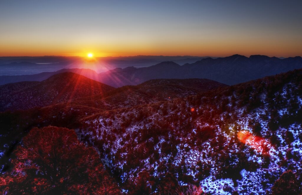 Sunset over rolling hills with vibrant orange light and snow patches reflecting rich colors Wallpaper