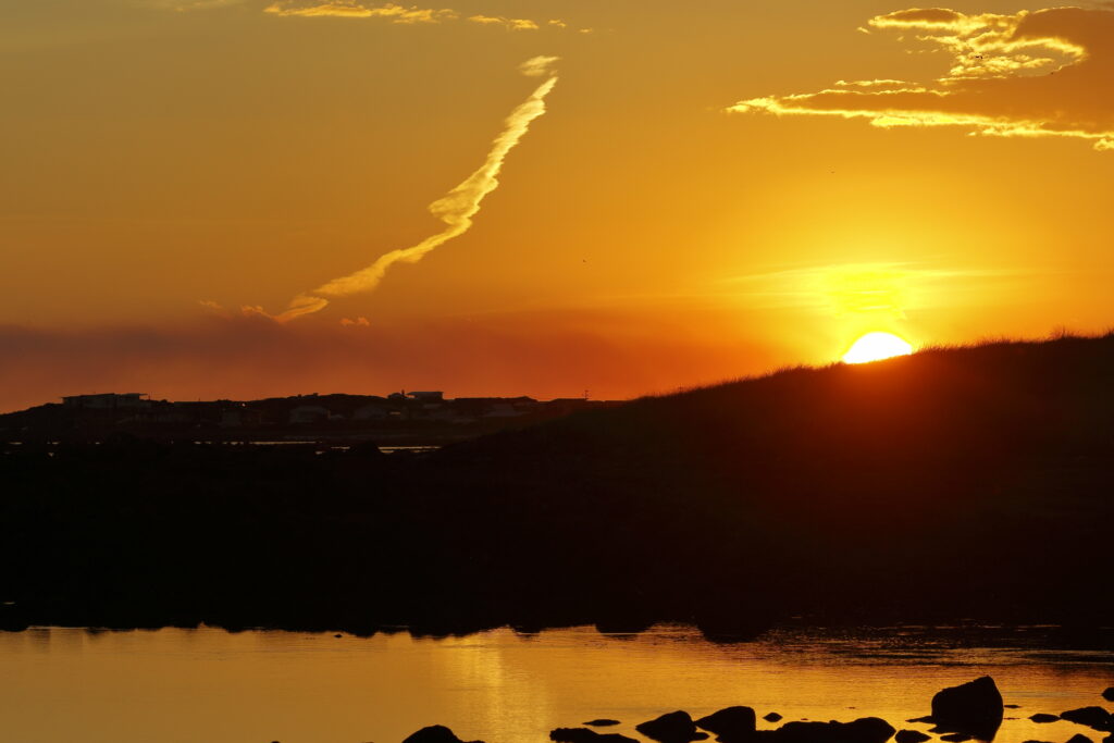 Sunset over tranquil seaside hill with golden hues and scattered stones reflecting on water Wallpaper