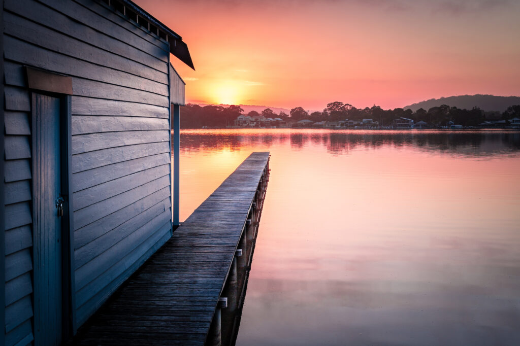 Tranquil pier over calm lake at sunset with warm orange pink purple sky reflection wallpaper