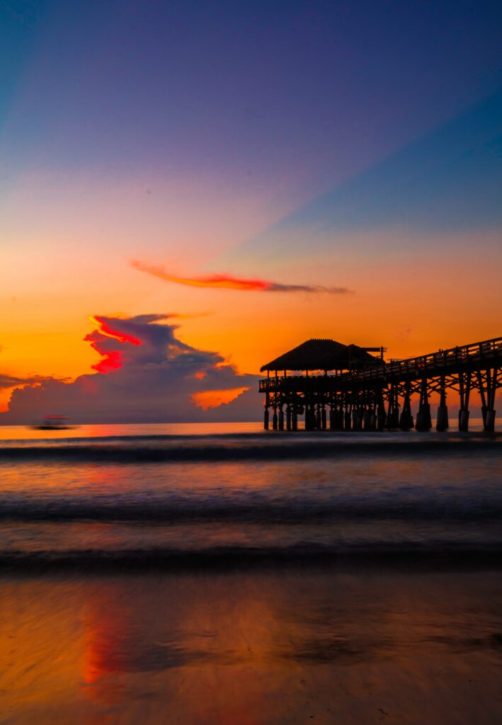 Sunset pier over calm surf with golden hues soft clouds reflecting on sea and sandy beach Wallpaper