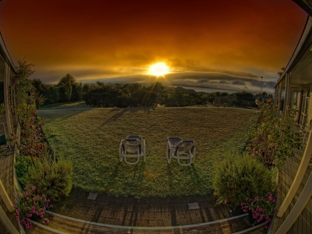 Empty porch chairs overlooking vibrant lawn at dramatic sunset peaceful evening wallpaper background