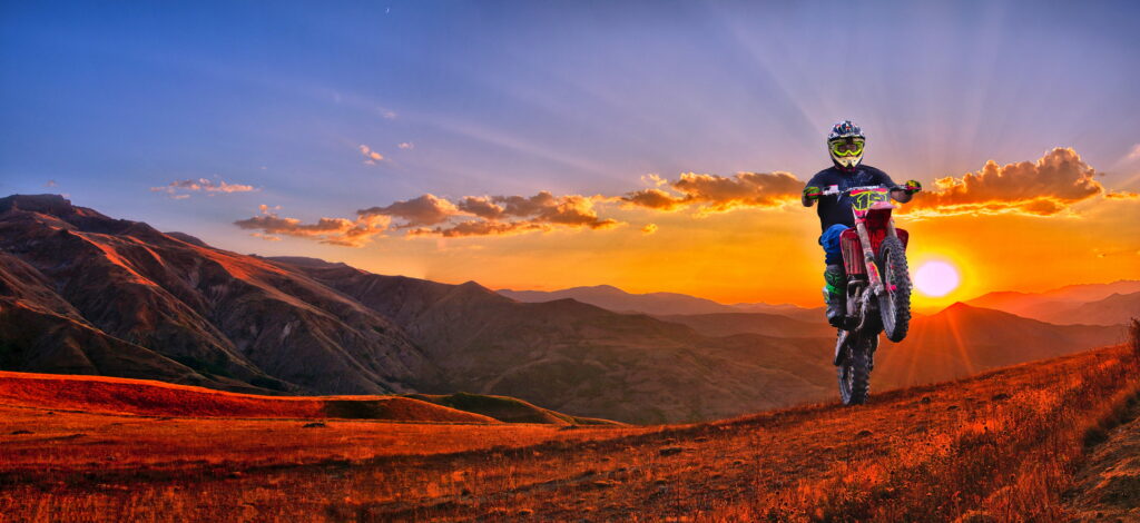 Sunset Adventure: Man Racing Through Panoramic Landscape on a Motocross Dirt Bike - Captivating 8K Wallpaper Background