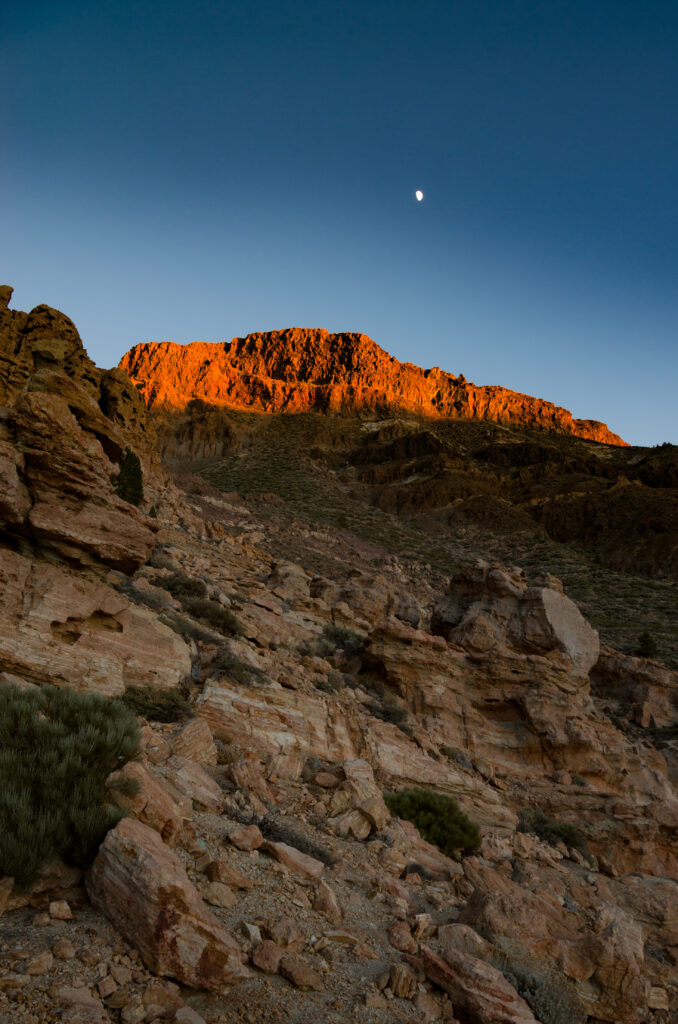 Rugged rocks at sunset with warm earth tones and a gentle moon in clear evening sky wallpaper