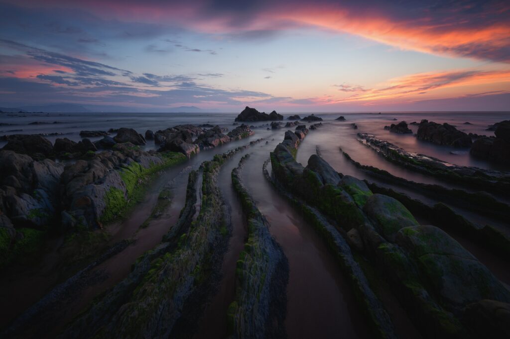 Sunset seascape of Barrika Spain with turbidite rock layers rugged coastline vibrant colorful sky Wallpaper