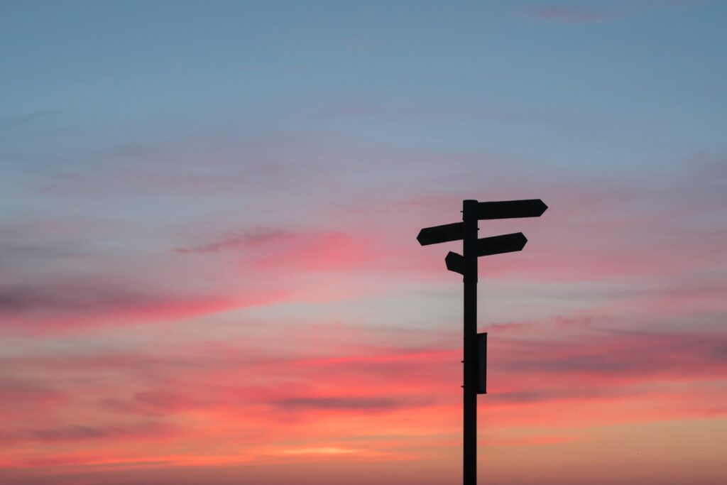 Silhouetted signpost with arrows against a pink and blue sunset sky symbolizing direction and choice Wallpaper