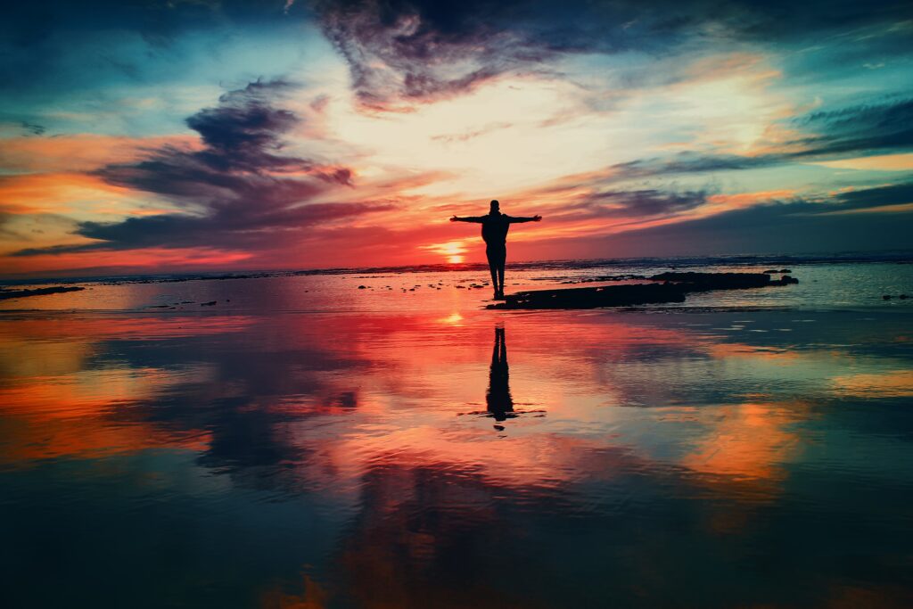 Silhouette with arms outstretched on shore at vibrant orange pink blue sunset inspiring freedom wallpaper