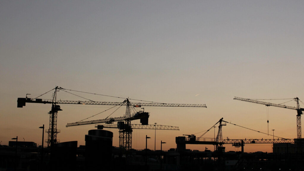 Silhouetted construction cranes at sunset showcasing urban development and city infrastructure Wallpaper
