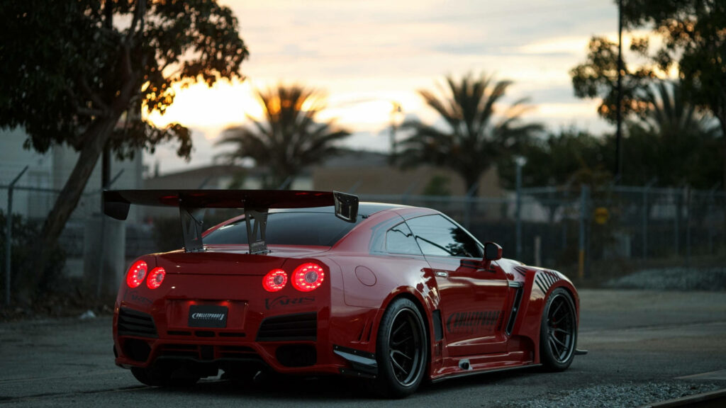 Blazing Trails: Capturing the Red GTR Speeding Through a Sunset-Filled Road, Surrounded by Trees Wallpaper