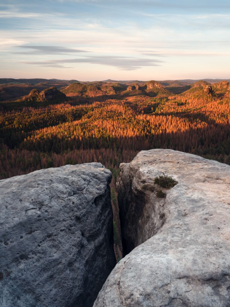 Rugged stone cliffs overlooking dense forest and colorful sunset hills serene nature landscape Wallpaper