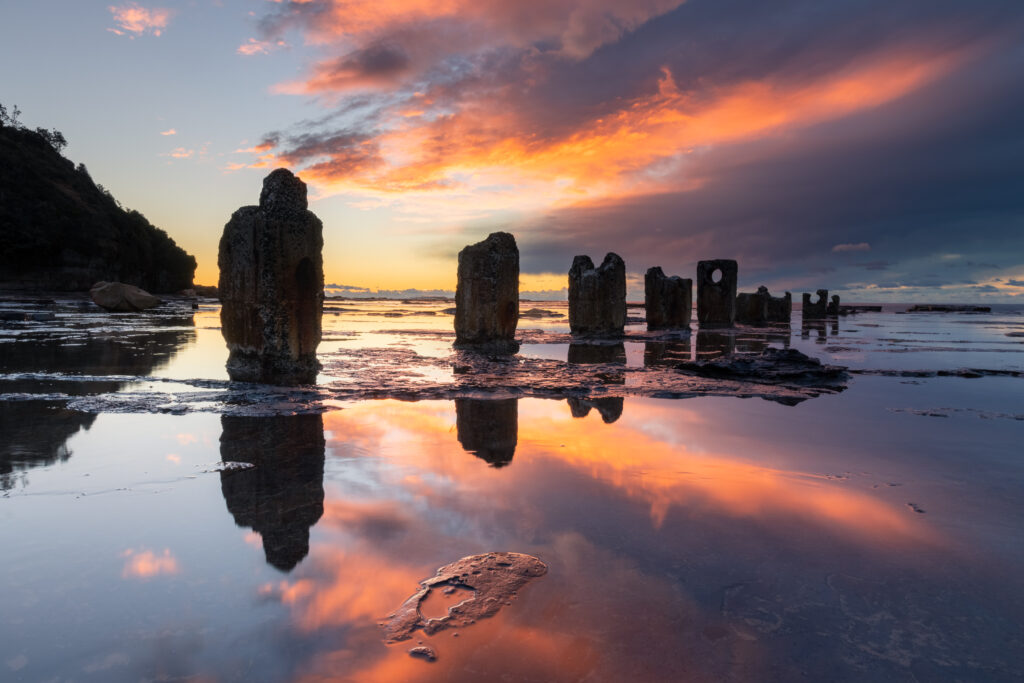 Weathered stone pillars reflected in calm water at vibrant sunset with deep blue and orange sky Wallpaper