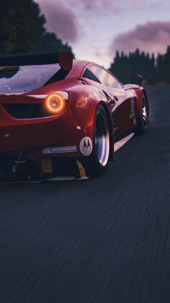 Roaring Red at Sunset: A Striking Ferrari 458 Slices Through the Black Pavement, Adorned with Michelin Sticker, as Lush Trees Line the Horizon - Captivating Car iPhone Wallpaper