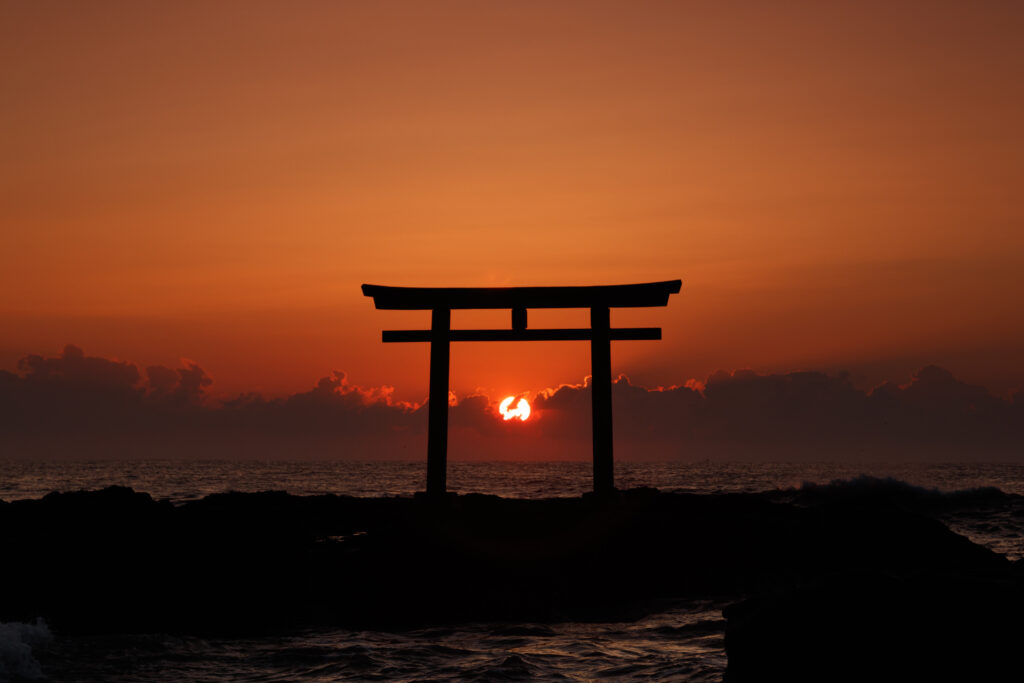Traditional torii arch silhouetted at sunset over sea vibrant orange sky serene cultural wallpaper