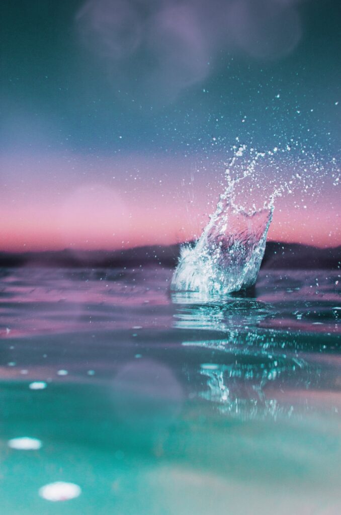 Vibrant water splash over calm surface at sunset with turquoise and pink hues wallpaper background