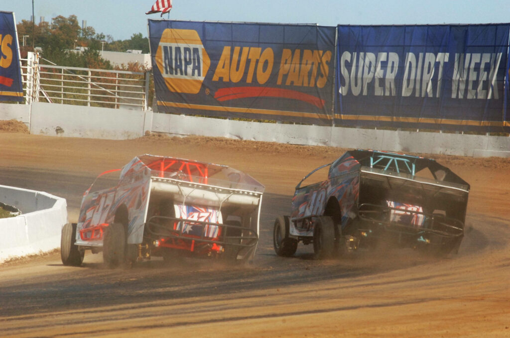 Two dirt cars race side by side kicking up dust during Super DIRT Week intense racing action Wallpaper