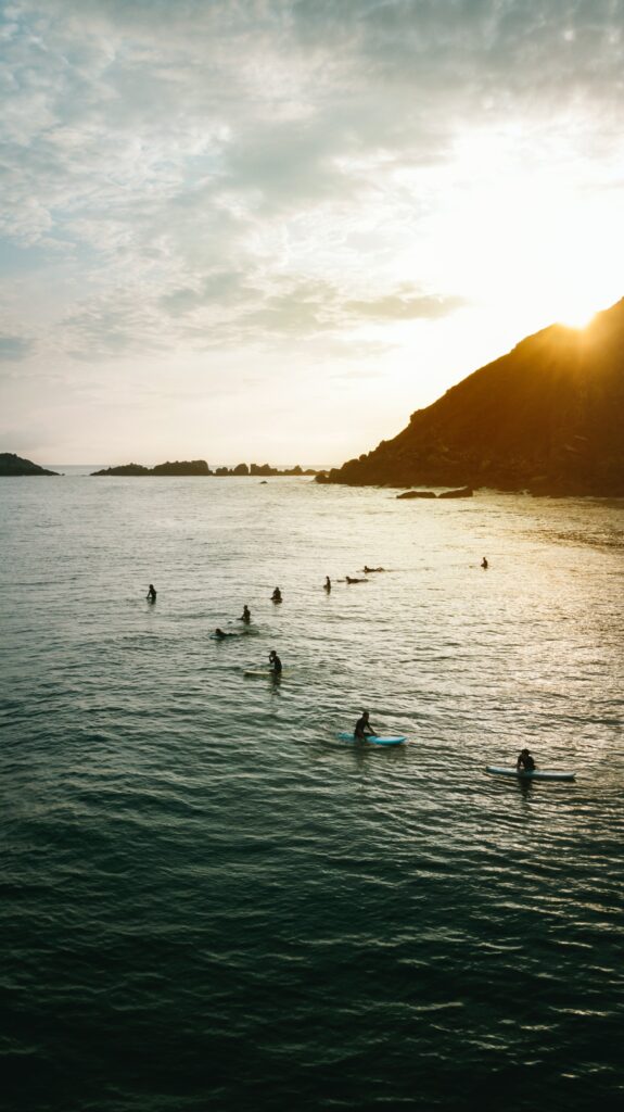 Surfers paddling on gentle waves near rocky coast at sunset golden light serene surfing scene Wallpaper