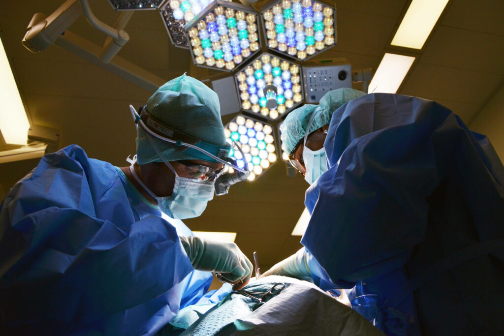 Two surgeons in blue scrubs performing surgery under bright lights in a modern operating room Wallpaper