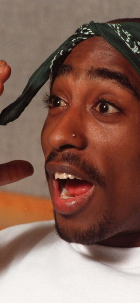 Surprising Expression Captured: iPhone-Ready Image of Tupac Shakur, the Celebrated American Rapper, Against an Intriguing Background Wallpaper