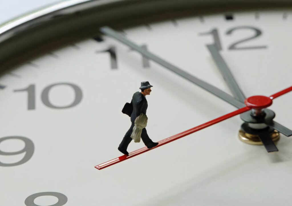 Miniature businessman figure on red clock hand symbolizing time urgency and daily routine Wallpaper
