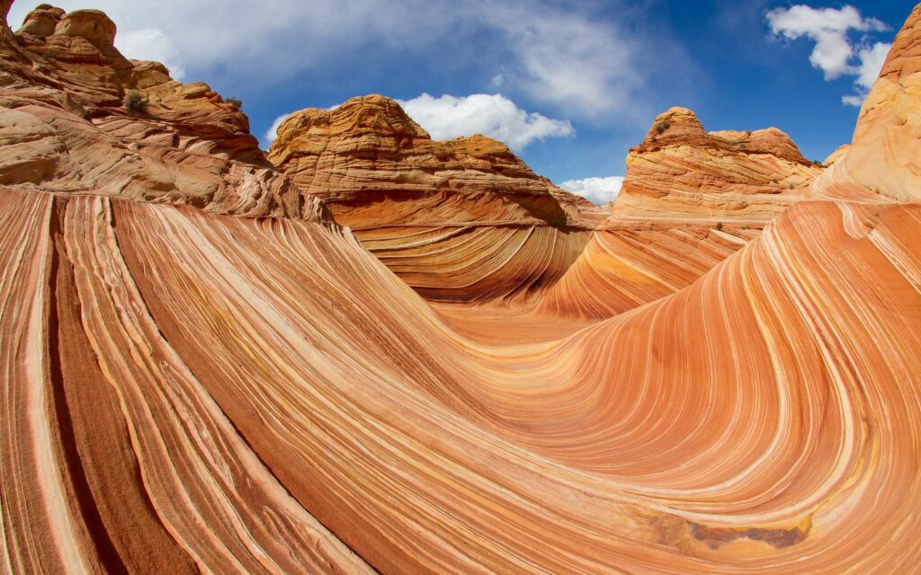 Stunning canyon wallpaper with flowing rock patterns in orange red and tan hues under blue sky