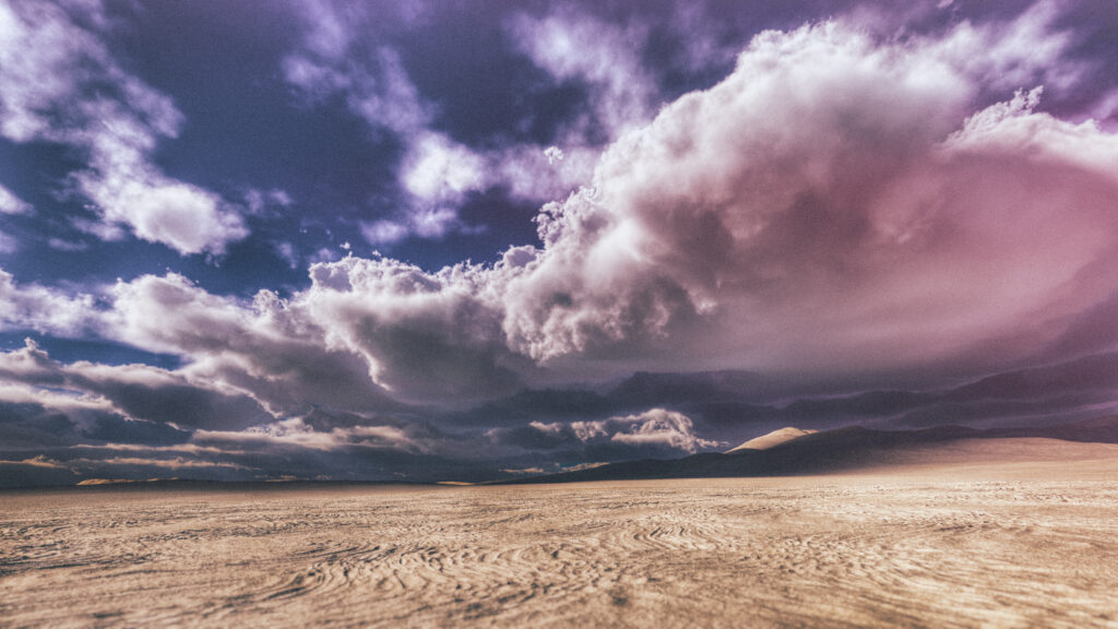 Surreal desert wallpaper with textured sand and vibrant purple white clouds under dramatic sky