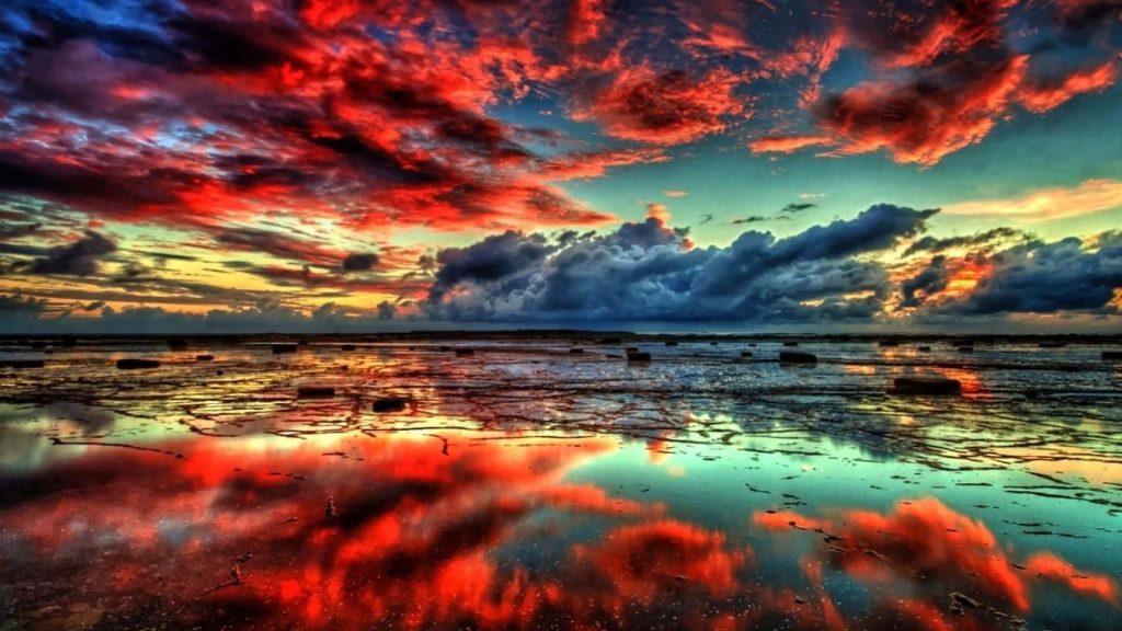 Surreal sunset with fiery red and blue clouds reflecting on rocky tidal flats desktop wallpaper