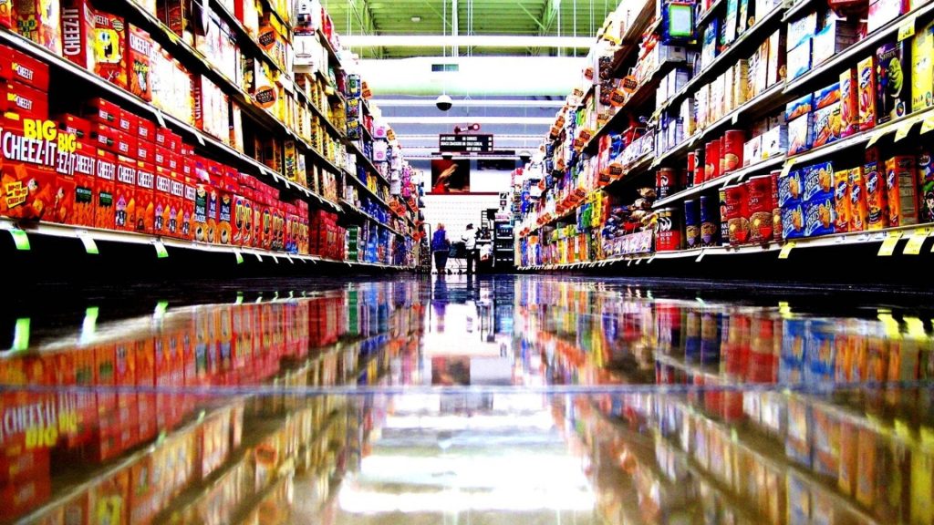 Low-angle grocery aisle with polished mirror floor vibrant snack shelves SpongeBob Shrek labels bright lights Wallpaper