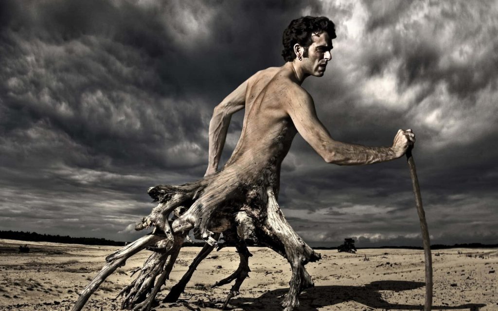 Surreal man fused with tree roots walking in barren desert under stormy dramatic sky wallpaper