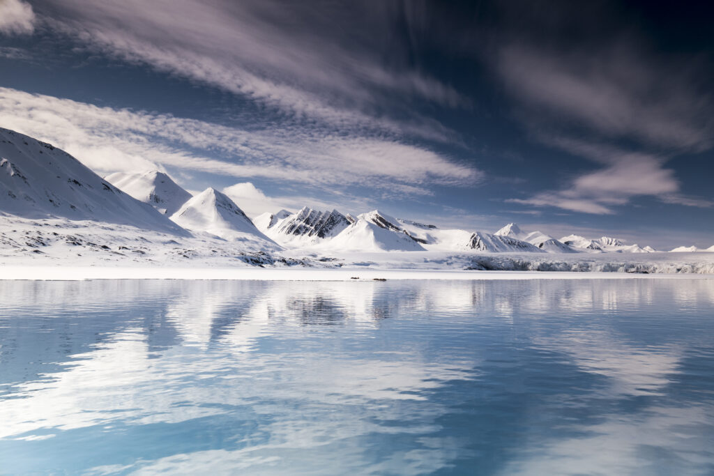 Snow-covered Svalbard mountains reflected in a blue lake under dramatic Arctic sky clouds wallpaper