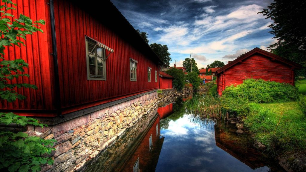 HD wallpaper of iconic Swedish red timber houses by canal with stone foundations and greenery