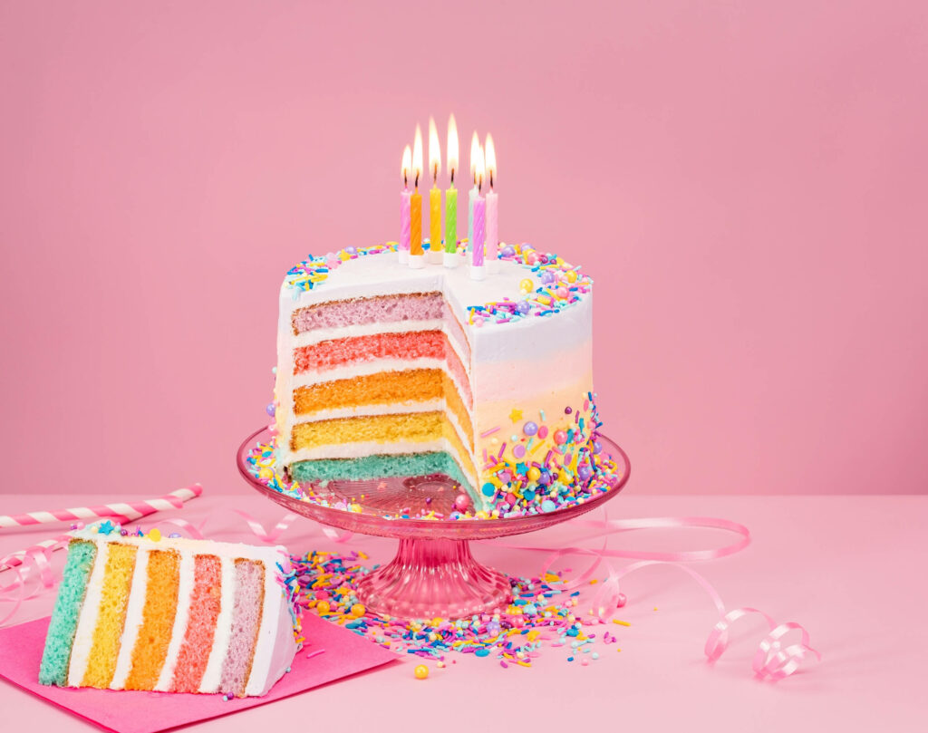 Whimsical Birthday Delight: Pastel Layered Cake Surrounded by Sweet Candles on a Pink Background Wallpaper