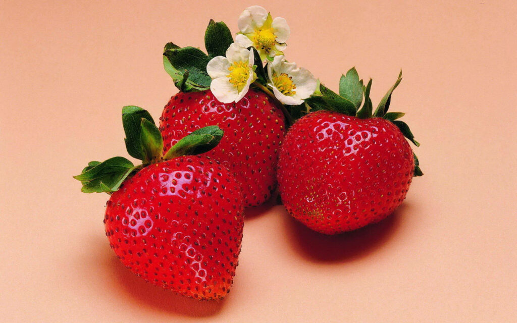 Sweet Delight: Three Pink Strawberries with Floral Accents on a Peach Background Wallpaper