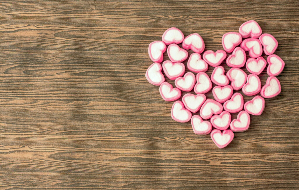 Heart-shaped marshmallows with pink edges arranged in a large heart on rustic wood background Wallpaper
