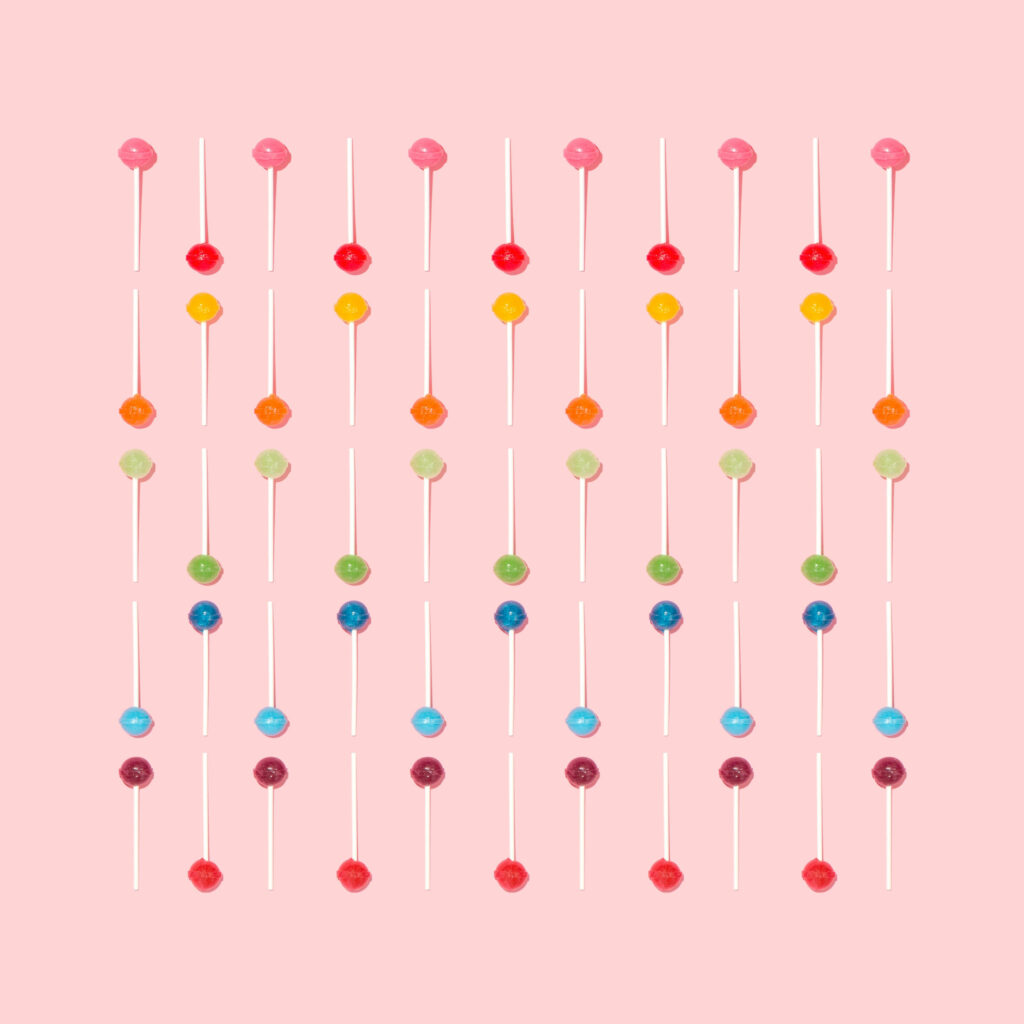 Sweet Delights: A Playful Ensemble of Multicolored Lollipops on a Pastel Pink Canvas - An Aesthetic Encounter Wallpaper