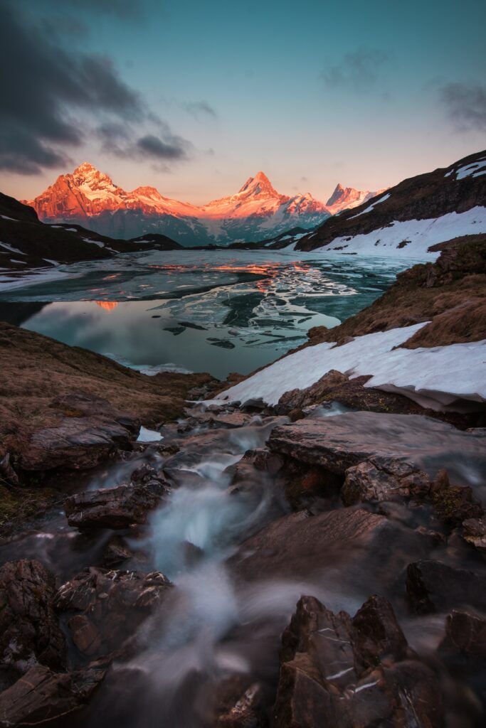 Swiss sunset landscape with snow-capped mountains reflected in icy lake and flowing water Wallpaper