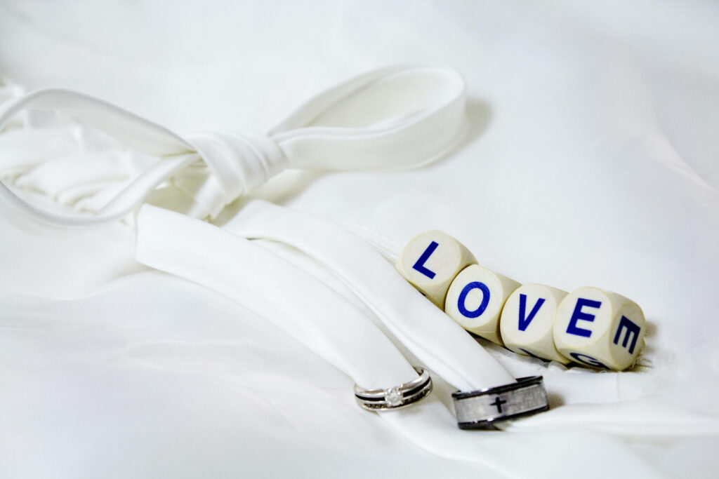 Two wedding rings on white silk beside blue wooden dice blocks spelling love wedding wallpaper background
