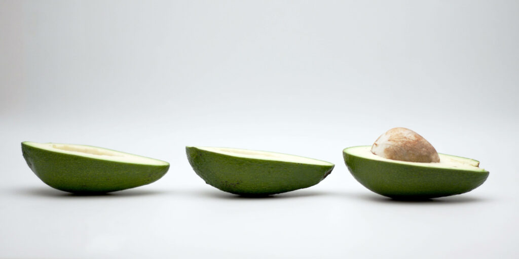 Captivating Composition of Split Avocado Halves with Intact Seed on a White Background Wallpaper