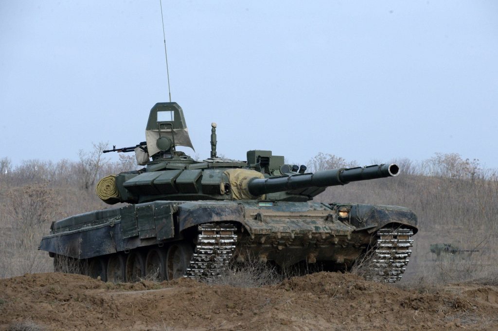 T-84 Oplot tank driving through muddy field under overcast sky realistic military wallpaper