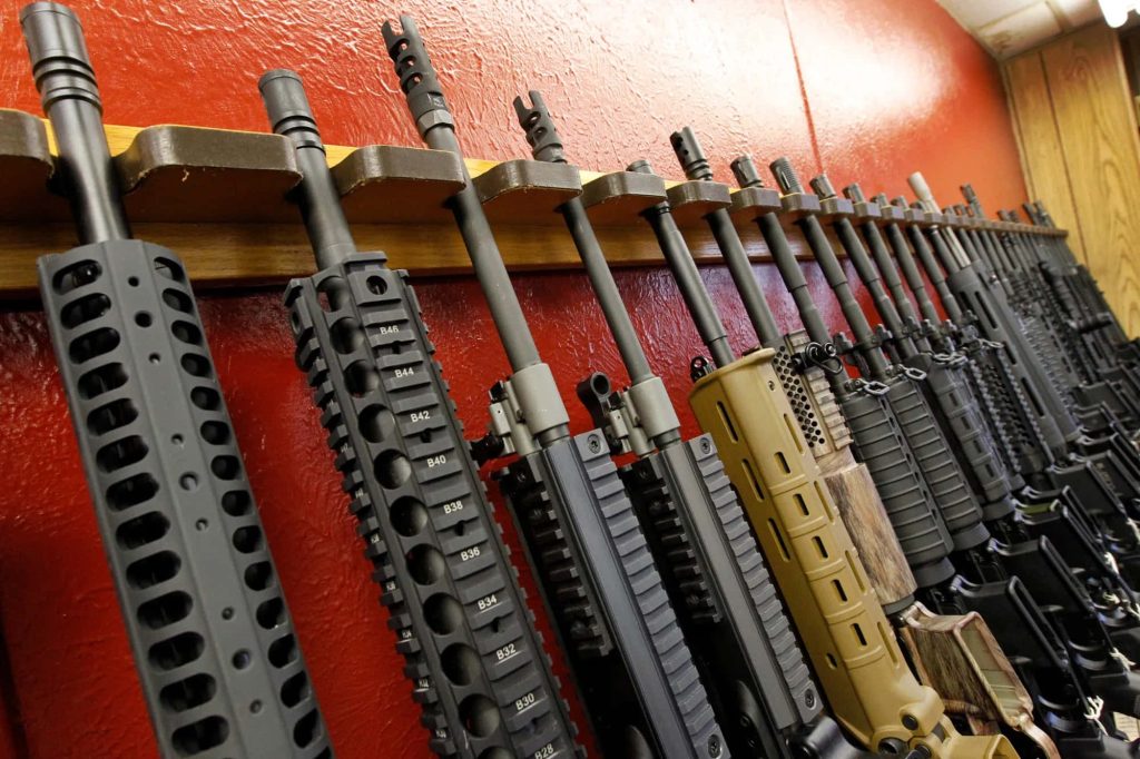 Rack of modern AR-style rifles with modular handguards on textured red wall wallpaper