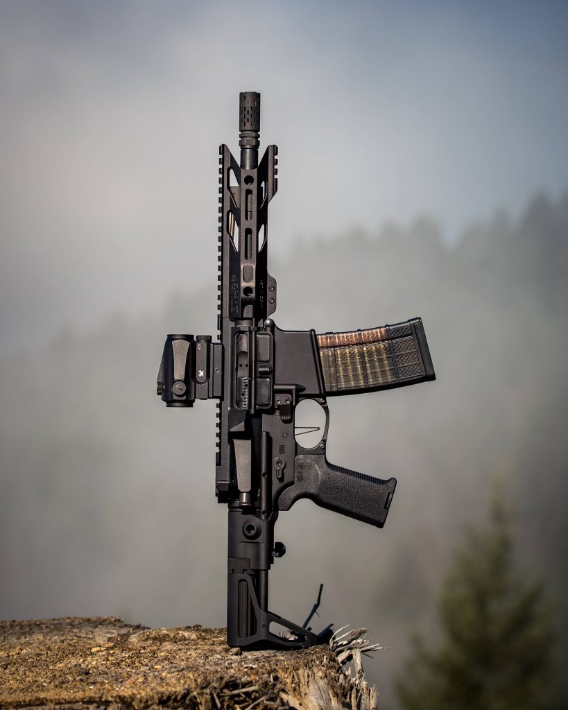 Tactical AR-15 rifle with Vortex optic on tree stump in misty mountain forest wallpaper background