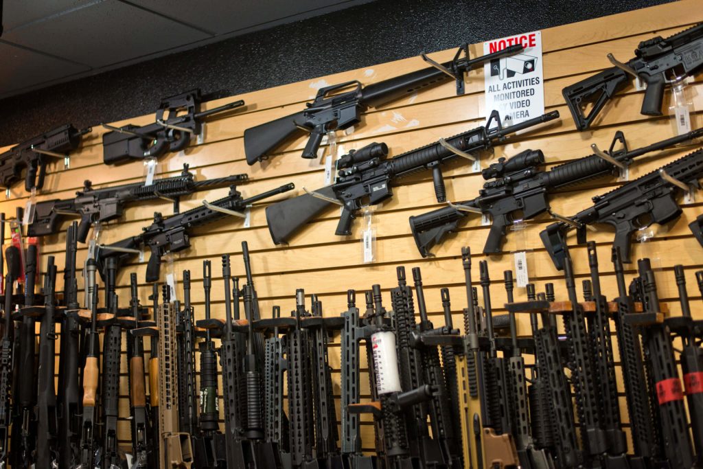 Tactical gun shop display with black rifles AR platform FN P90 on wooden slat wall surveillance sign Wallpaper