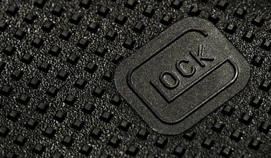 Close-up of Glock logo on textured black polymer grip showcasing tactical firearm craftsmanship Wallpaper